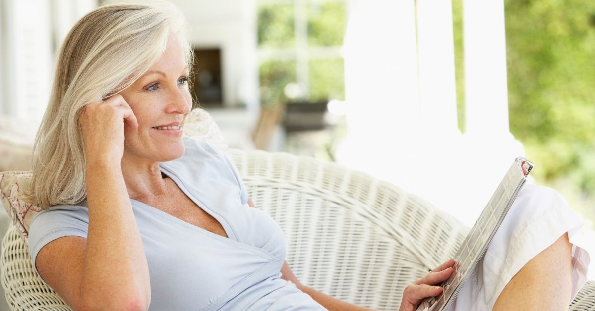 Mature woman relaxing on a porch with a magazine, smiling thoughtfully – symbolizing self-reflection, confidence, and emotional maturity in relationships