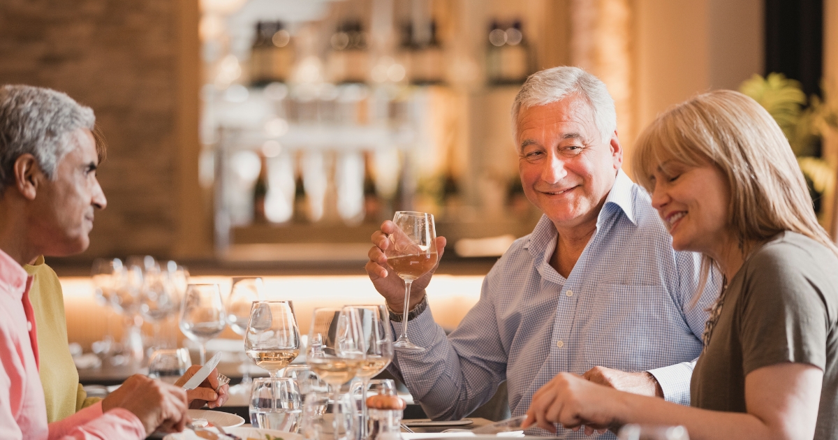 Group of older adults enjoying wine and conversation at a stylish restaurant — representing socializing and meeting new people over 50.