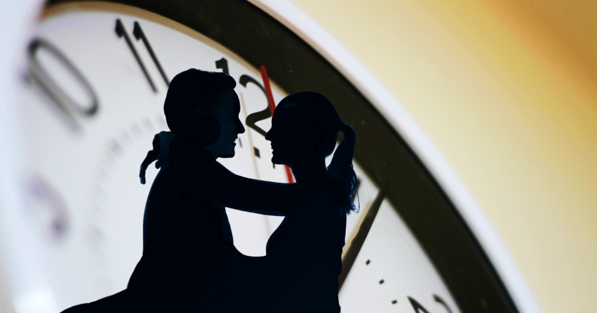 Silhouette of a couple embracing in front of a large clock, representing timing and frequency in dating relationships