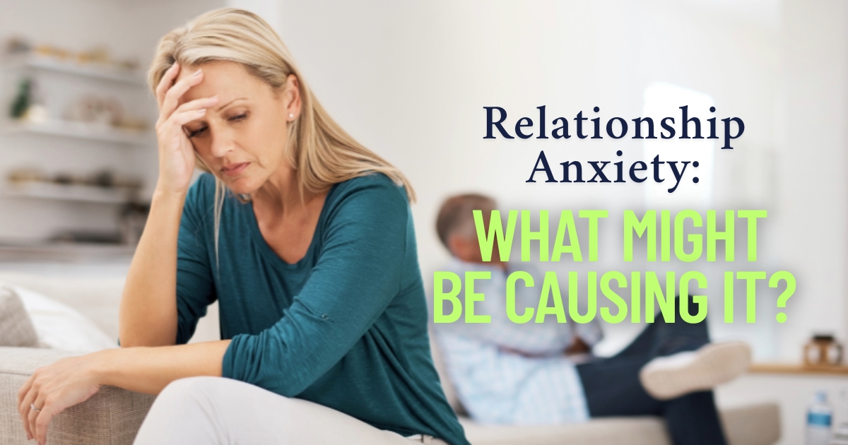 Middle-aged woman sitting on a couch looking stressed with her hand on her forehead, while a man sits in the background; overlaid text reads 'Relationship Anxiety: What Might Be Causing It?
