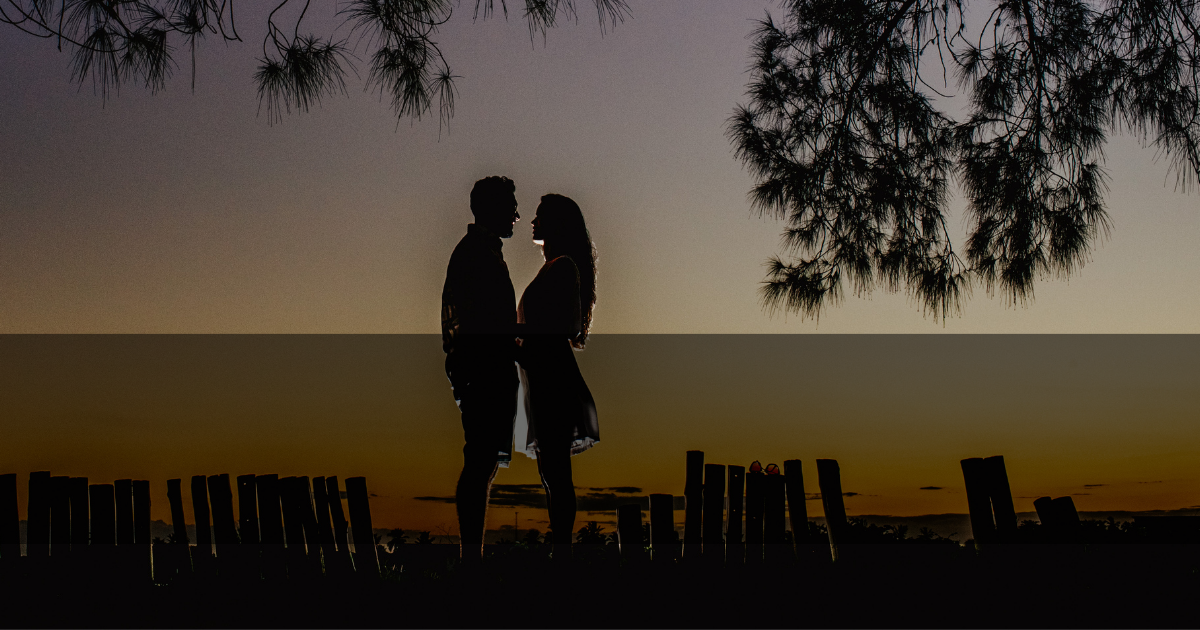 5 Ways To Get A Mans Attention - Mature Singles Finding Love Silhouette of a couple standing close together at sunset, surrounded by trees and wooden fences, evoking a romantic and serene atmosphere.
