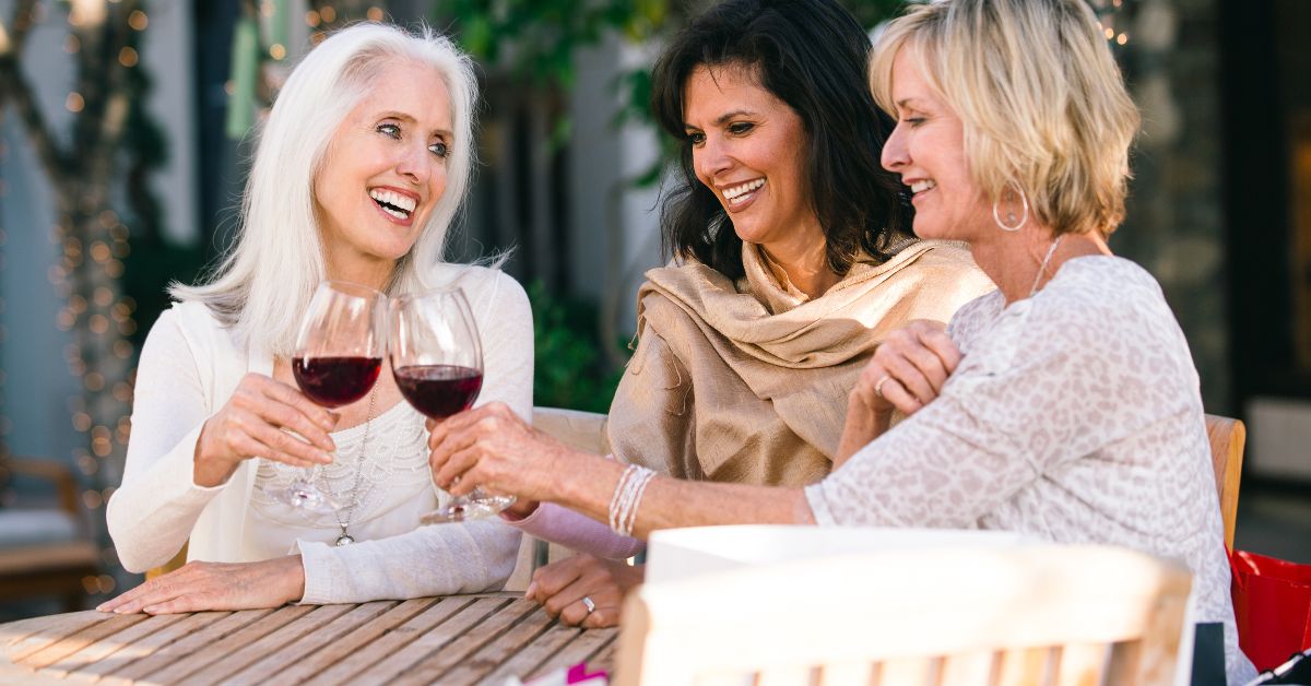 Group of joyful older women toasting with wine, celebrating friendship and support after relationship challenges