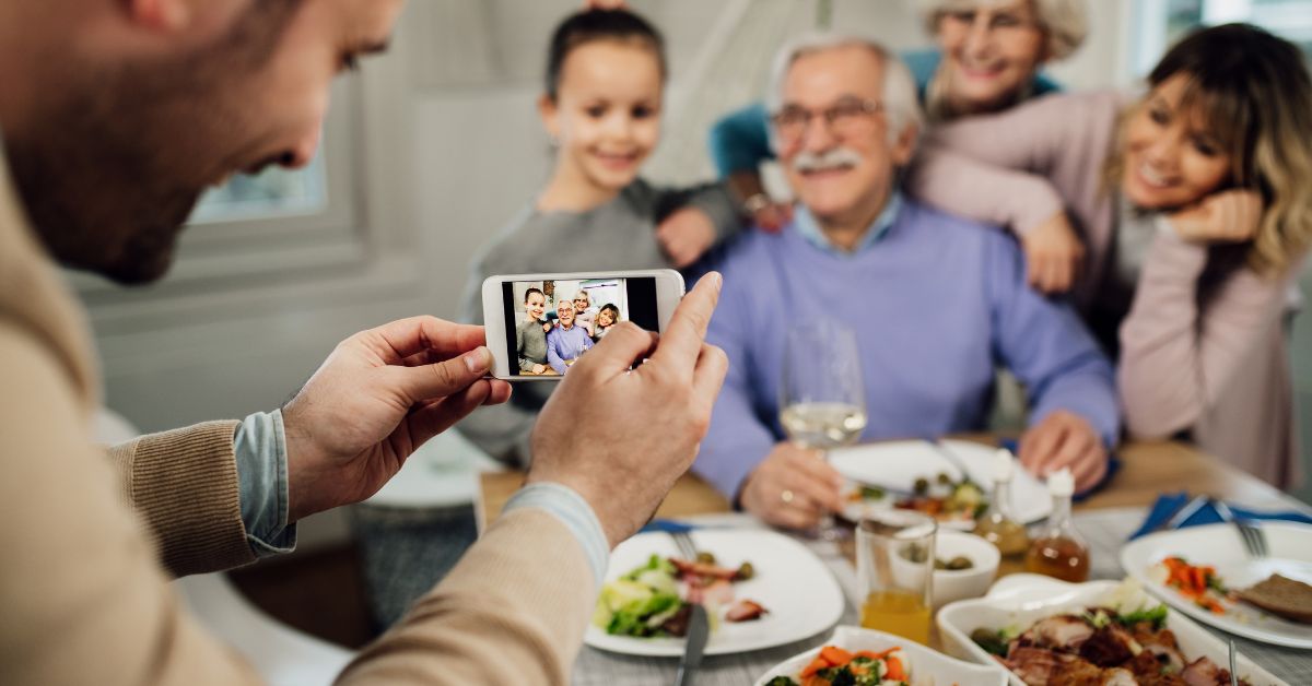 Man taking a family photo during a joyful meal, symbolizing bonding moments and celebrating blended families after 50.