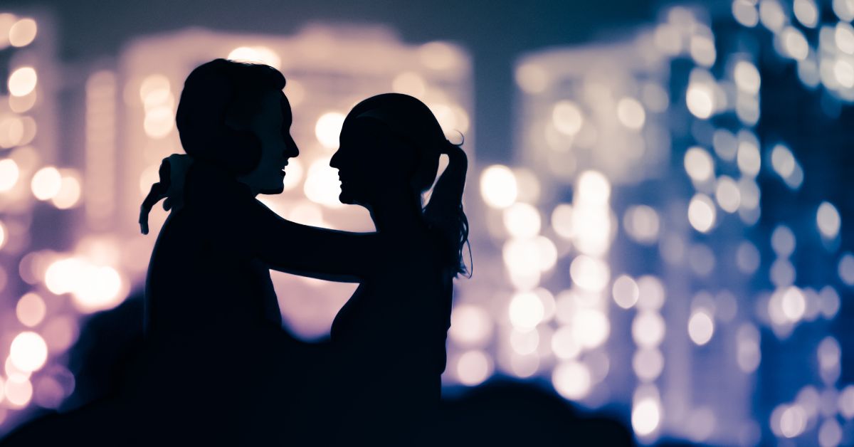Silhouetted couple embracing against a blurred city lights backdrop, symbolizing romance and emotional connection.