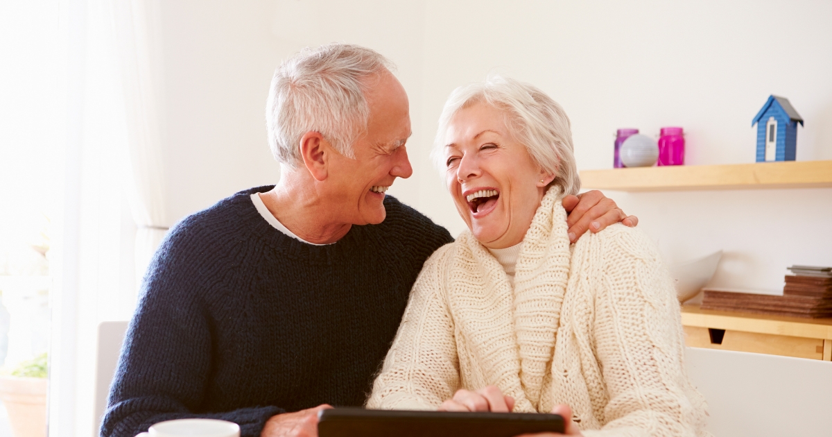 Dating at Any Age_ A Guide to Finding Love in Your Golden Years - Mature Singles Finding Love Happy senior couple laughing together at home while using a digital tablet, symbolizing love, companionship, and connection in their golden years.