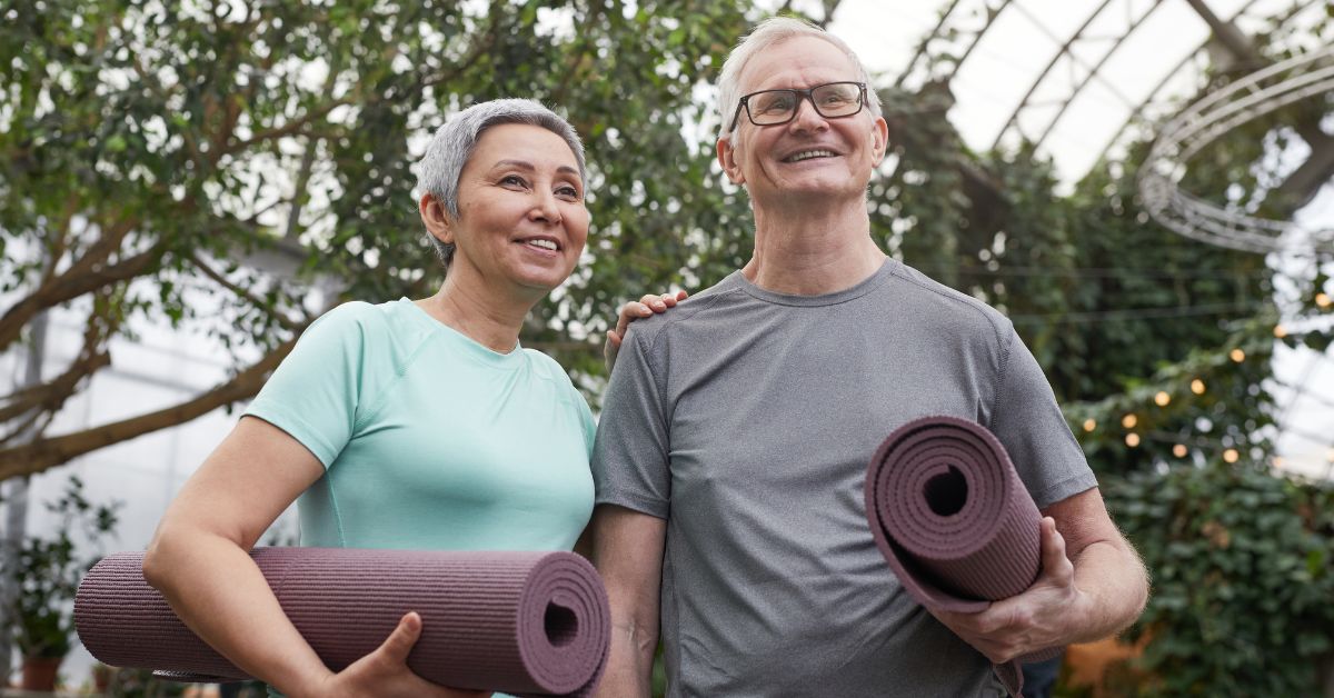 Happy senior couple holding yoga mats in an indoor garden, symbolizing active lifestyle and companionship in dating over 50