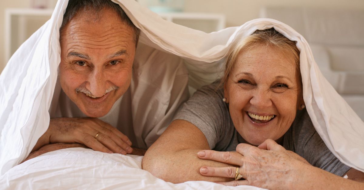 Happy older couple enjoying intimate moment in bed under blanket