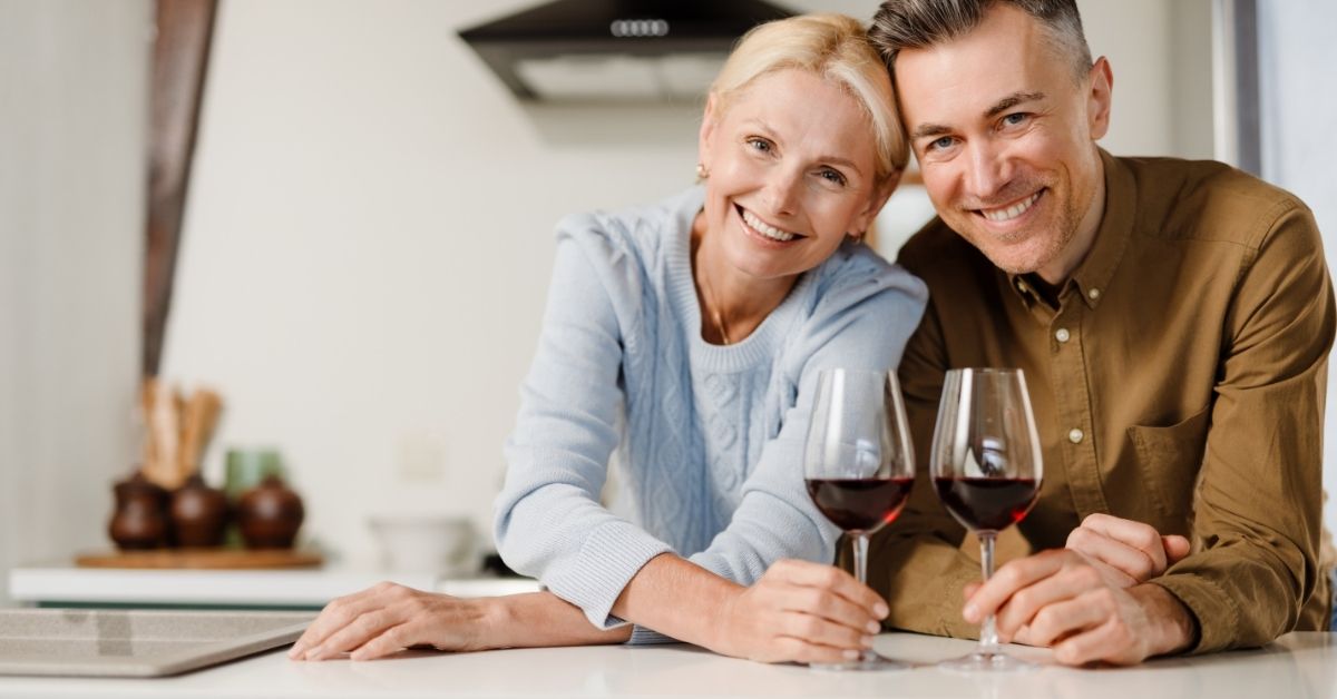 Empowering Your Passion_ Celebrating a Thriving Sex Life in Later Years - Mature Singles Finding Love Happy mature couple enjoying a glass of red wine together in a modern kitchen, symbolizing emotional connection and romantic intimacy in later years.