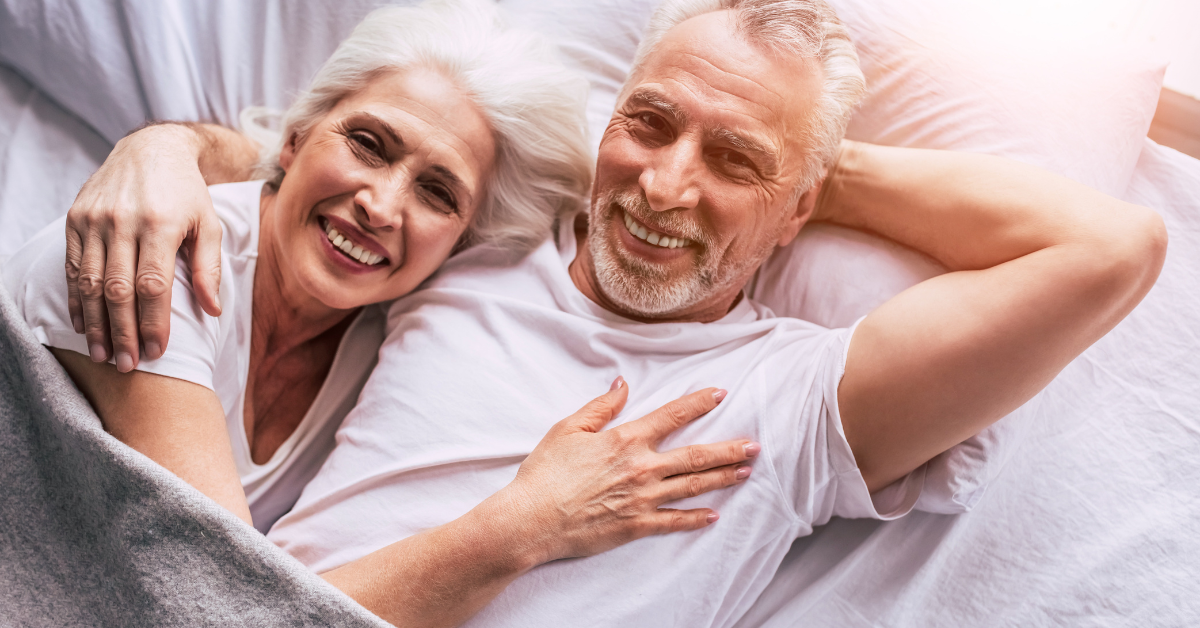 Joyful senior couple cuddling in bed, smiling and embracing each other, representing intimacy, affection, and a thriving sex life in later years.
