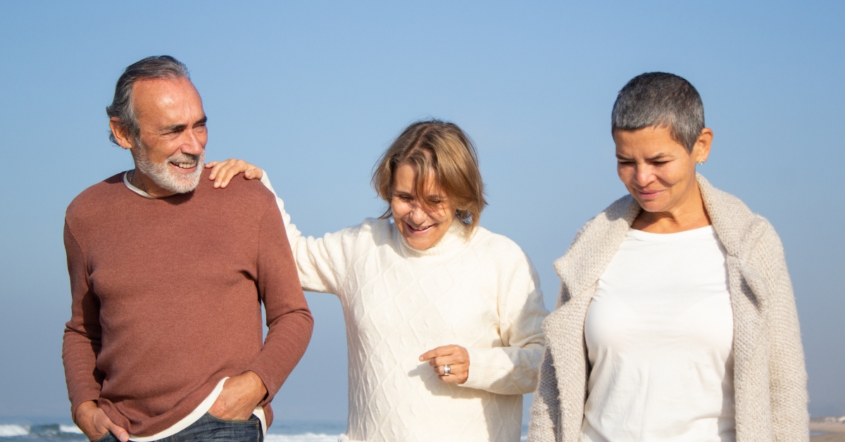 Exploring Polyamory_ Dating Tips for Beginners - Mature Singles Finding Love Happy mature polyamorous couple walking on the beach with a partner, representing ethical non-monogamy and polyamory dating over 50.