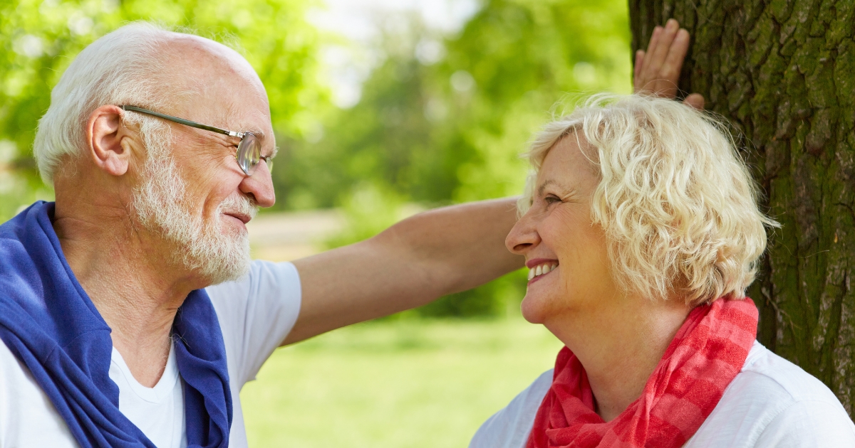 Flirting at 50+_ Rekindling Confidence and Fun - Mature Singles Finding Love Happy senior couple smiling and flirting outdoors under a tree, representing confidence and connection in dating after 50.