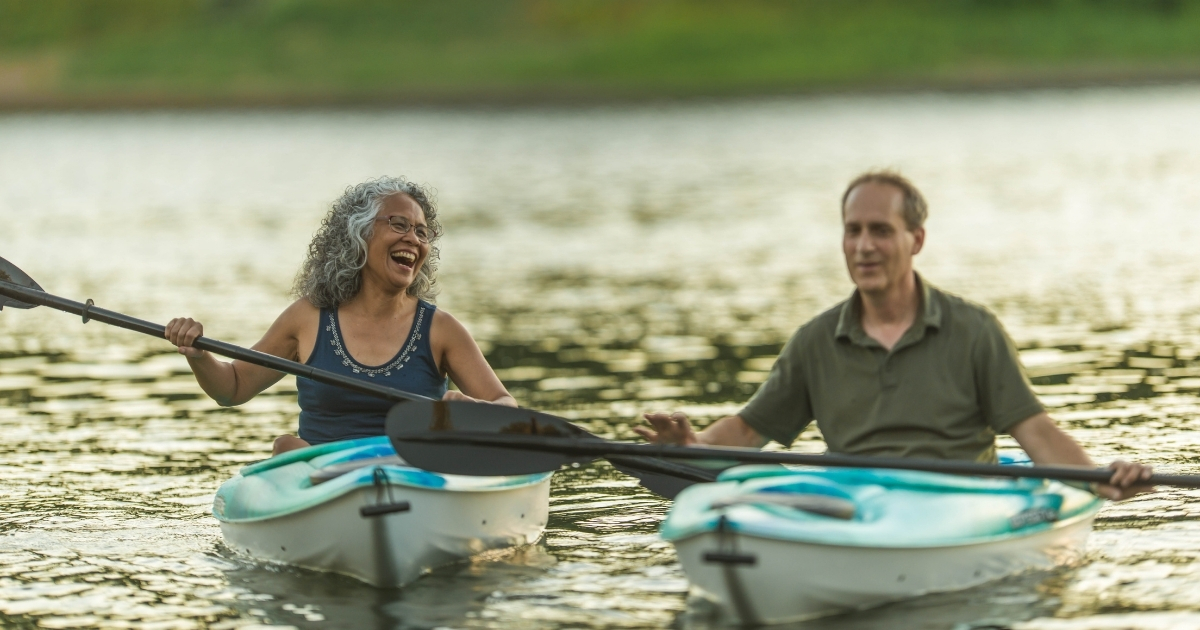 How Outdoor Activities Can Boost Your Health and Happiness - Mature Singles Finding Love Smiling older couple kayaking together on a calm lake, enjoying outdoor activities for health and happiness after 50.