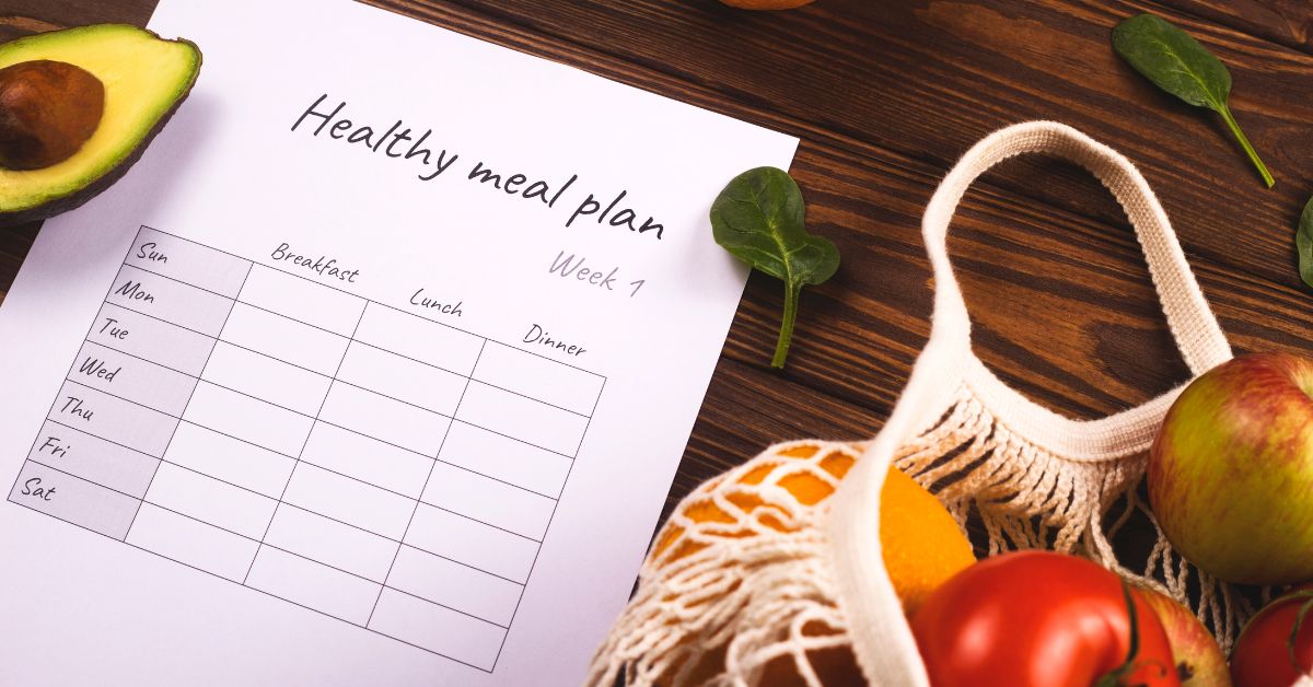 How to Create a Delicious and Healthy Weekly Meal Plan for One or Two - Mature Singles Finding Love Healthy weekly meal plan template on a wooden table surrounded by fresh fruits, vegetables, and a reusable produce bag.