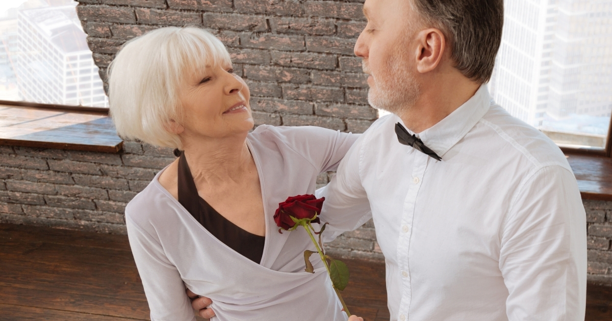 Older couple dancing together, sharing a romantic moment with a rose.