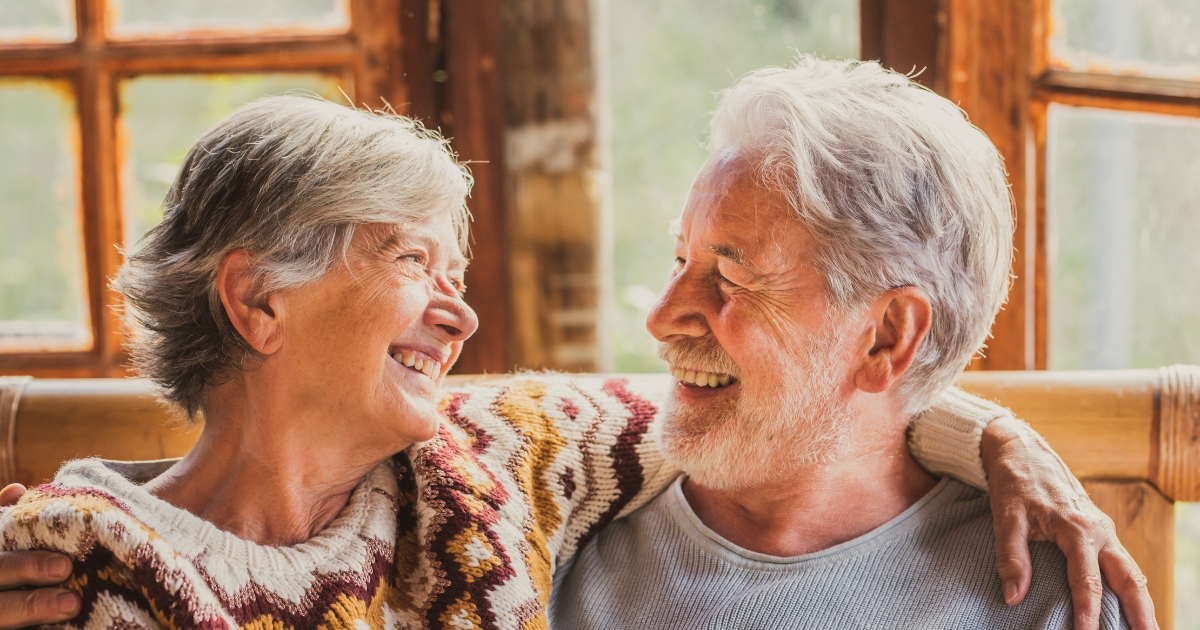 Smiling senior couple sitting close together, embracing and enjoying a warm moment, representing companionship and love in later life.