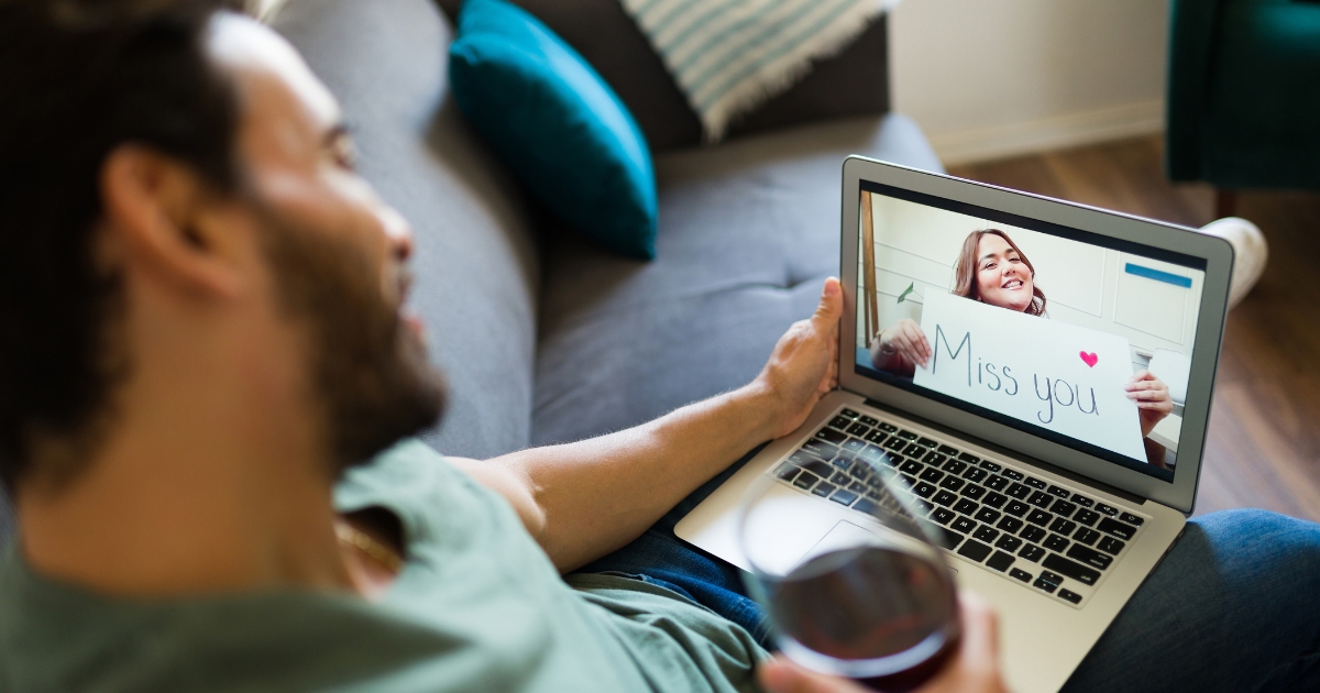 Man video chatting with a woman holding a 'Miss you' sign during an online date, showing connection and emotion in long-distance or separated relationships.