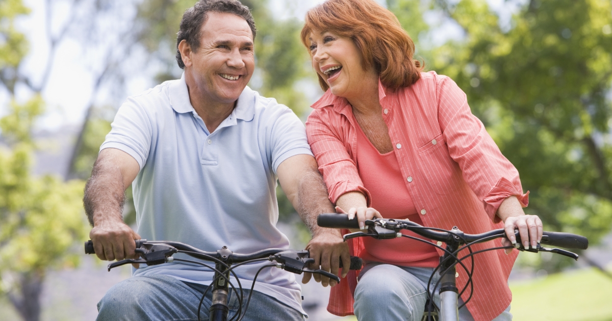 Smiling older couple riding bicycles together in a park, enjoying each other’s company on a sunny day.
