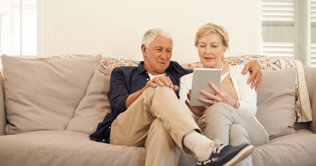 Senior couple sitting on a couch using a digital tablet together in a cozy home environment.