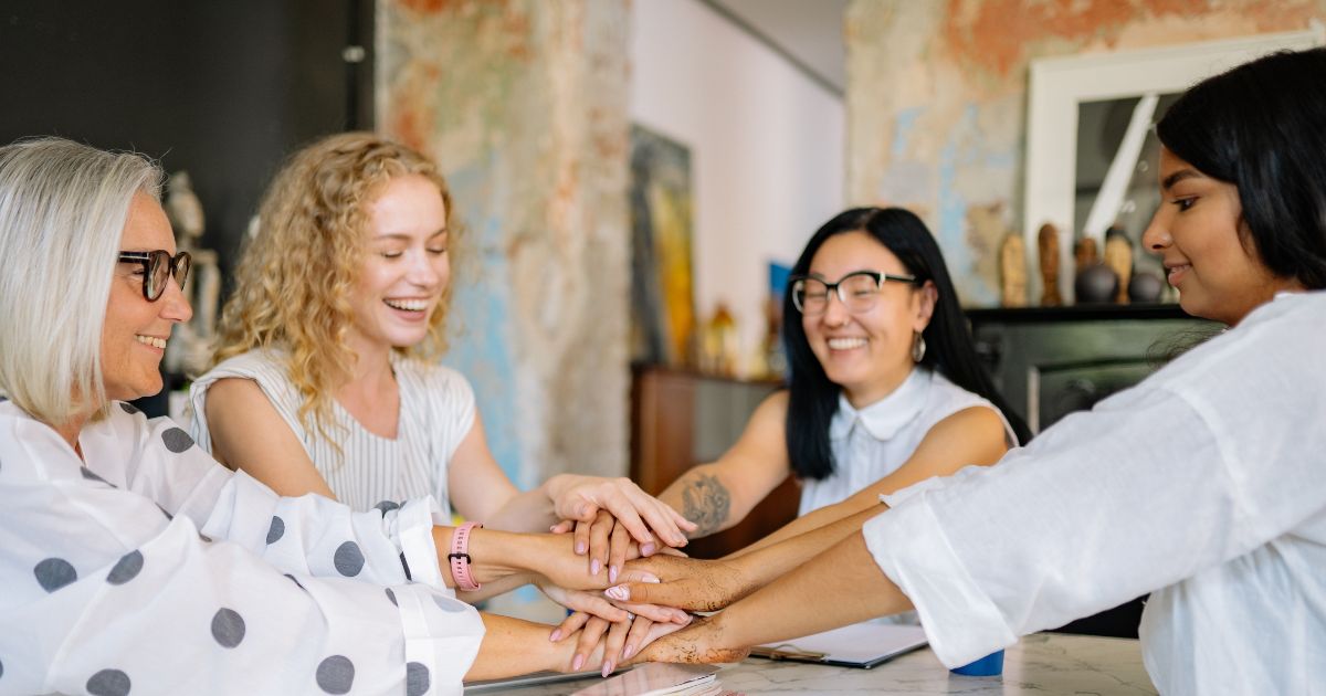 Diverse group of women smiling and stacking hands together in a show of teamwork and unity.