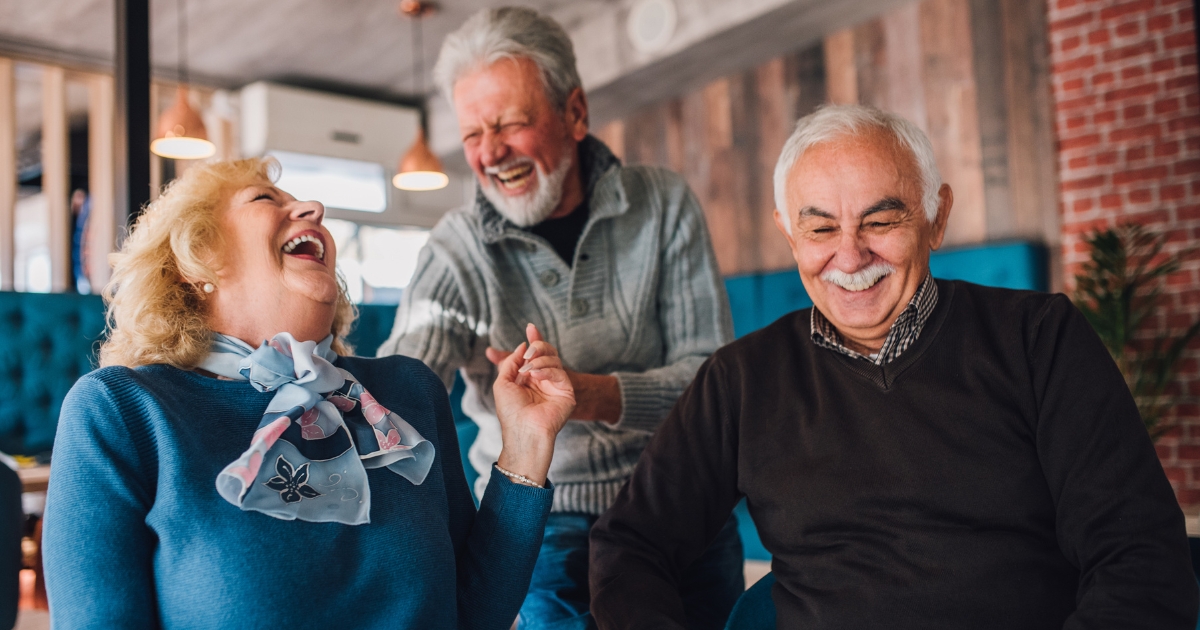 Group of happy older adults laughing together in a cozy café, representing joyful social connection and dating after 50.