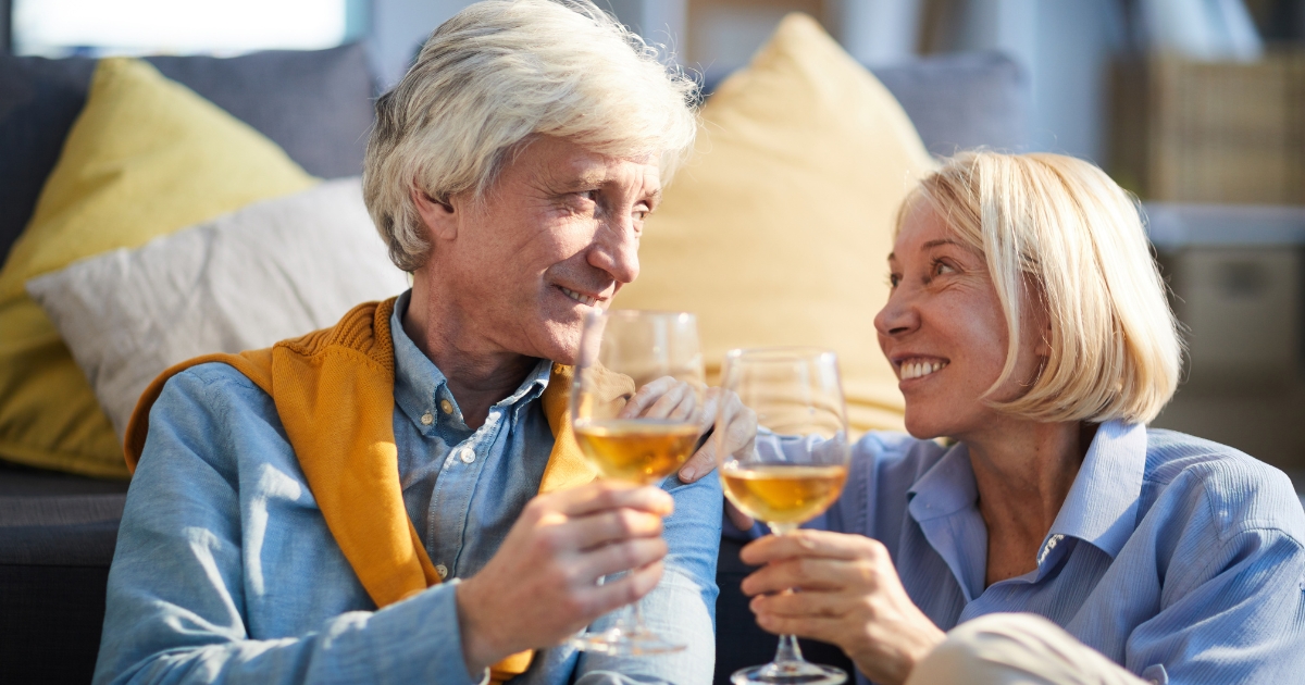 Happy mature couple smiling and toasting with wine glasses while sitting together, symbolizing connection, romance, and dating over 50.