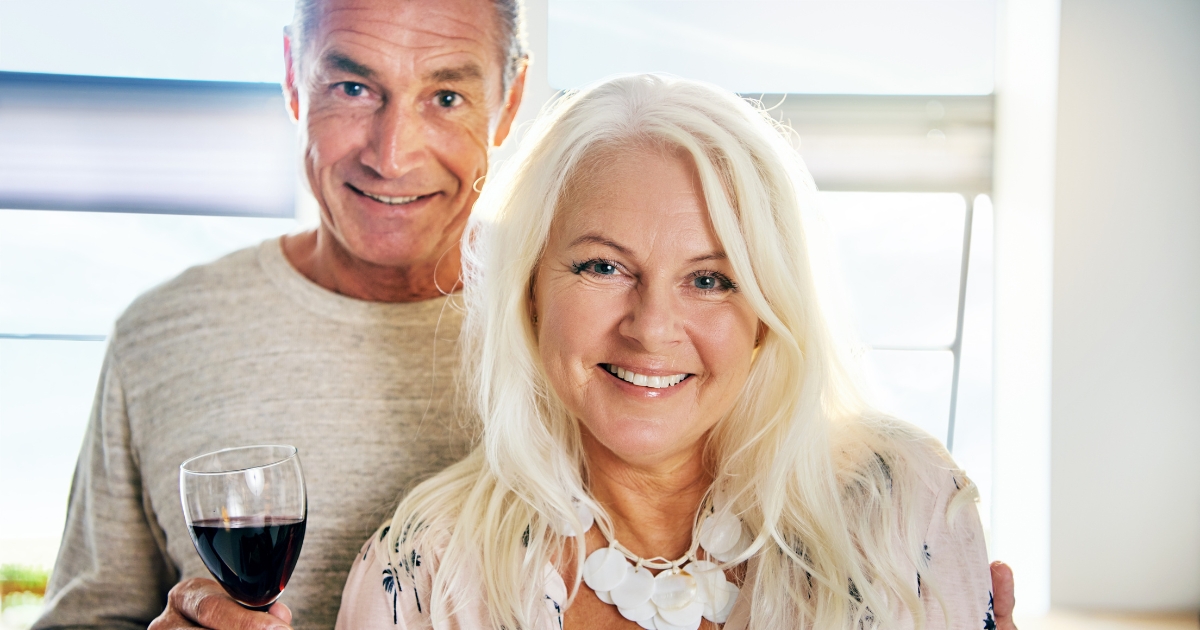 Happy senior couple enjoying a romantic moment together, with the man holding a glass of red wine and the woman smiling warmly—symbolizing love and connection in later life.