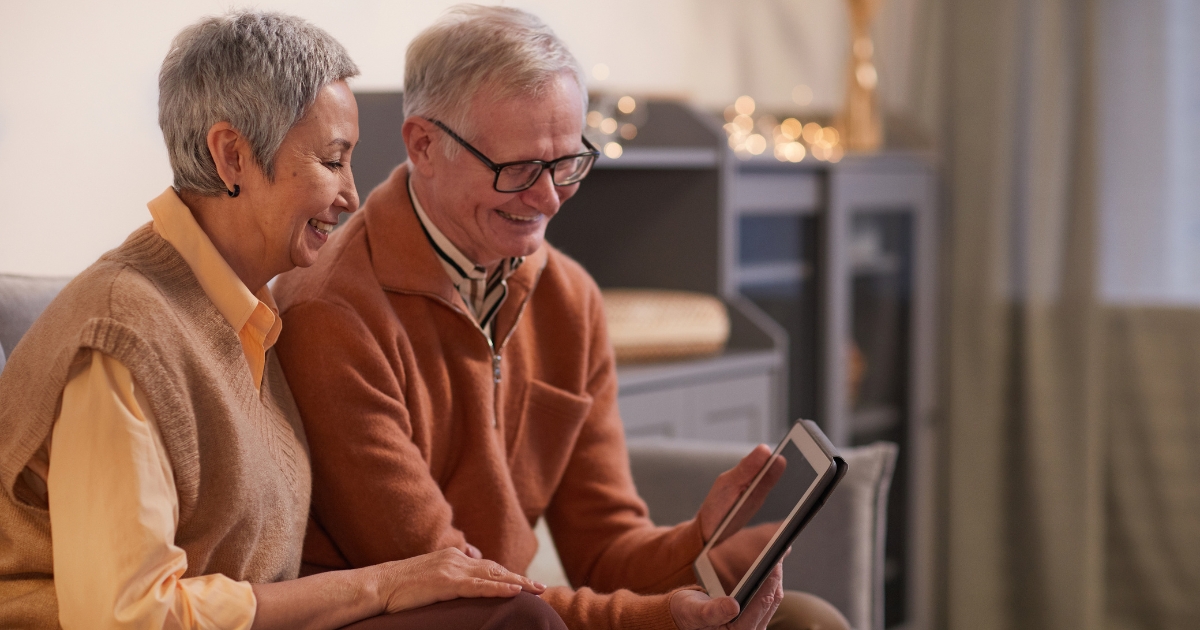 Happy senior couple sitting together on a couch and looking at a tablet