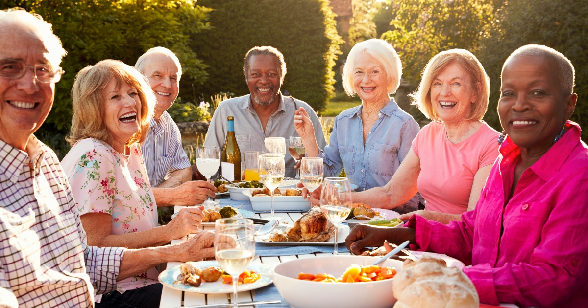 Group of happy older adults enjoying an outdoor meal together, representing social connection, companionship, and joyful relationships in later life.