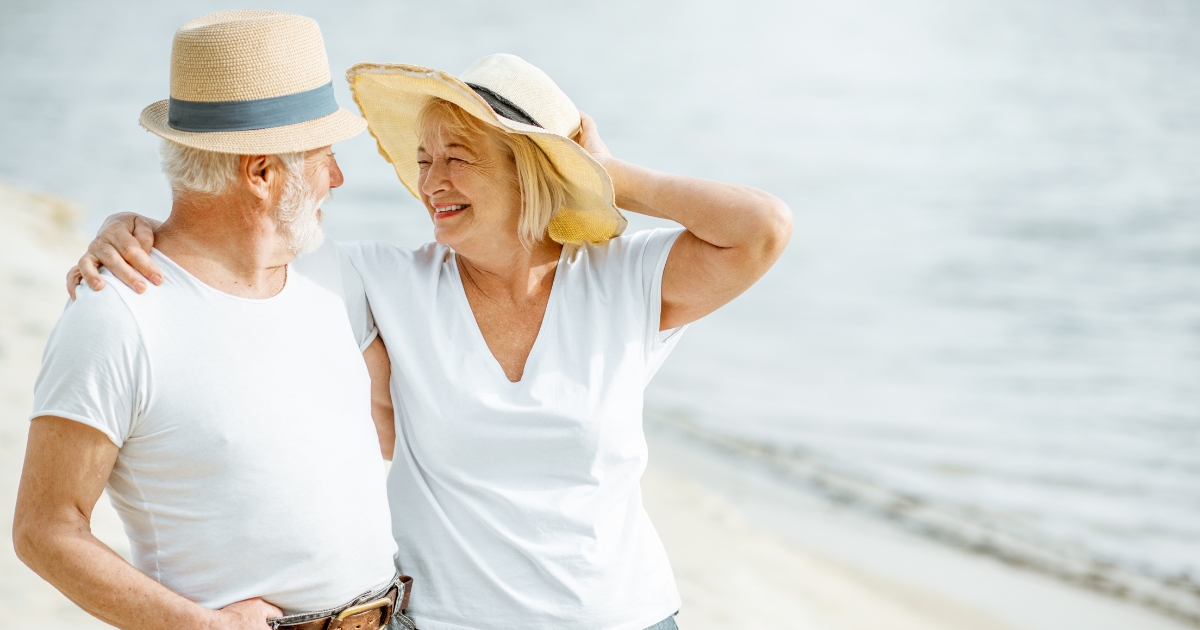 Smiling senior couple walking on the beach, embracing and enjoying quality time together, symbolizing balance in mature relationships.