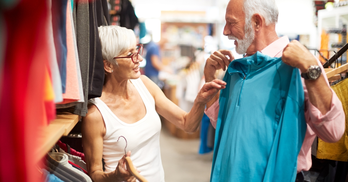 Happy older couple shopping for clothes together, smiling and engaging while picking out outfits—symbolizing confidence, companionship, and joyful dating after 50.