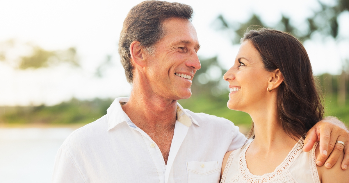 Happy mature couple smiling at each other while standing outdoors, showing emotional connection, trust, and lasting love in a romantic relationship.