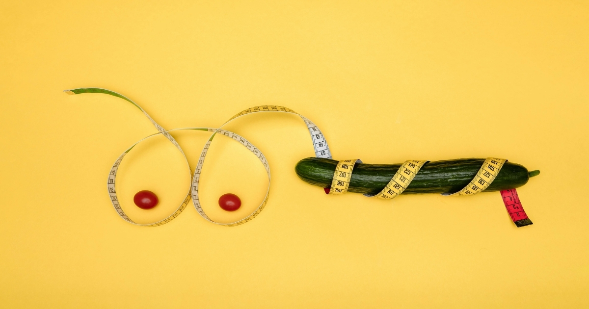 Playful sexual health concept using cucumber, cherry tomatoes, and measuring tape on yellow background