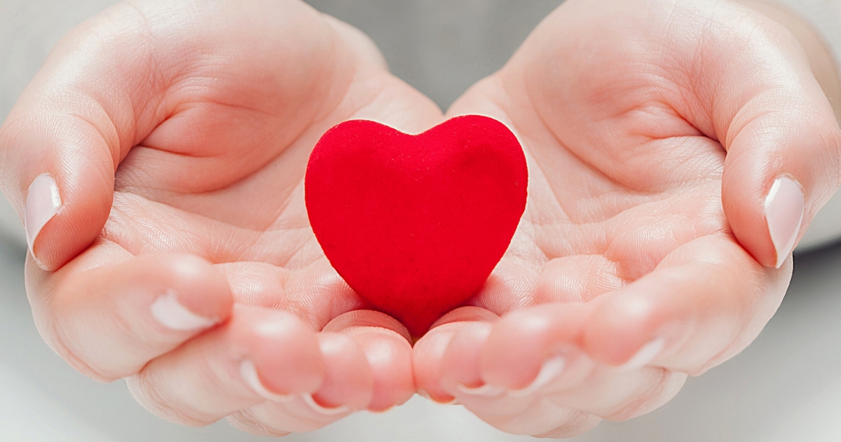Hands gently holding a red heart symbolizing love, care, and emotional vulnerability