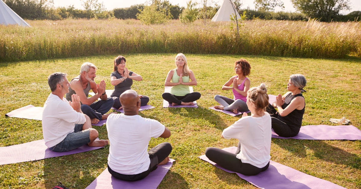 Group of mature adults meditating outdoors in a circle during a mindfulness session in nature.