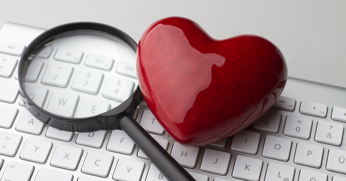 Red heart and magnifying glass resting on a white computer keyboard, symbolizing online dating and the search for love in the digital age.