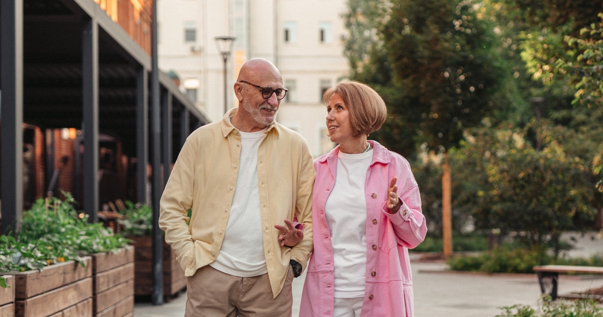 Smiling senior couple walking together outdoors, having a warm conversation, representing dating and connection later in life.
