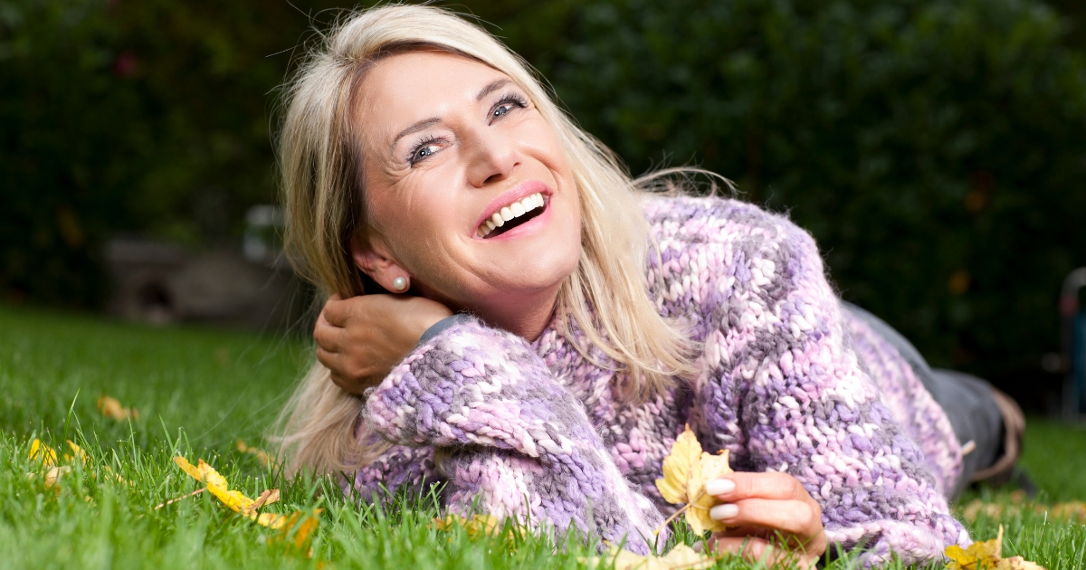 Joyful mature woman lying on grass in autumn, smiling and embracing life after 50.