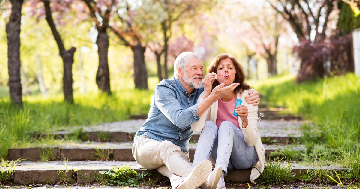 Happy mature couple blowing bubbles and enjoying a playful moment in a spring park, symbolizing love and joy after 50.