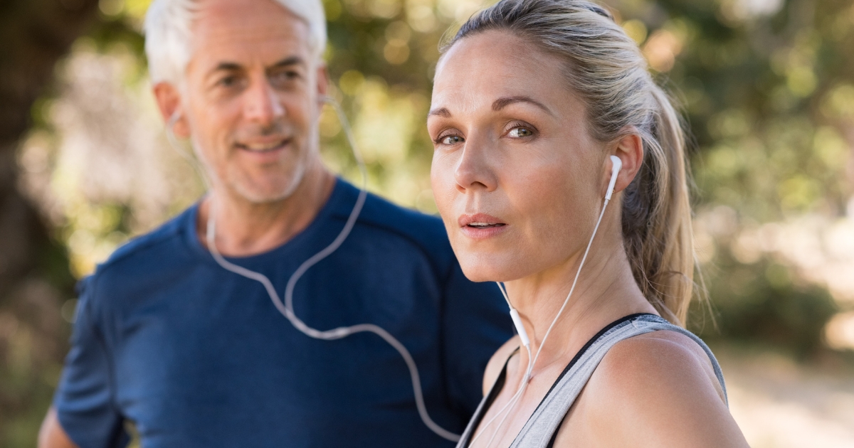Active mature couple outdoors wearing workout clothes and earphones, symbolizing healthy lifestyle, communication, and connection in midlife relationships.