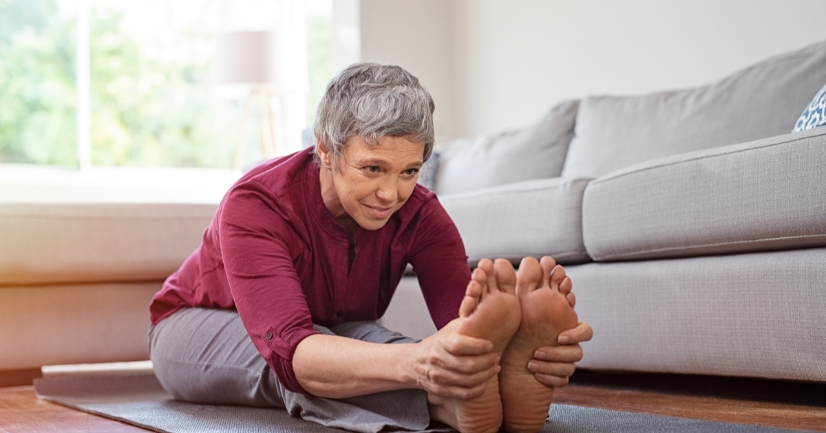 Senior woman stretching on yoga mat at home, focusing on flexibility and fitness for women over 50.