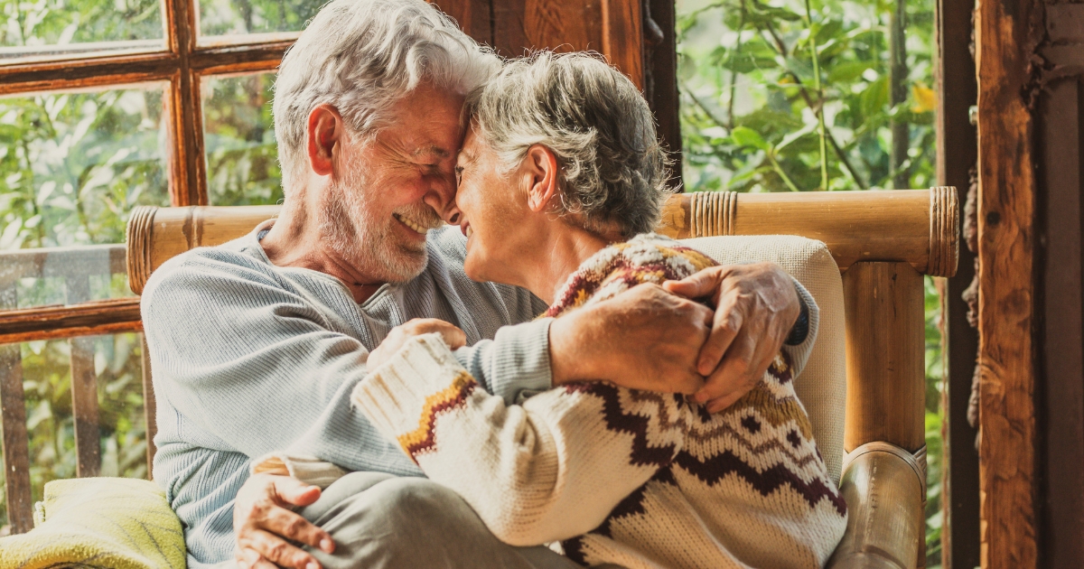 Affectionate senior couple cuddling and smiling indoors, showing warmth, love, and emotional intimacy in midlife relationships.