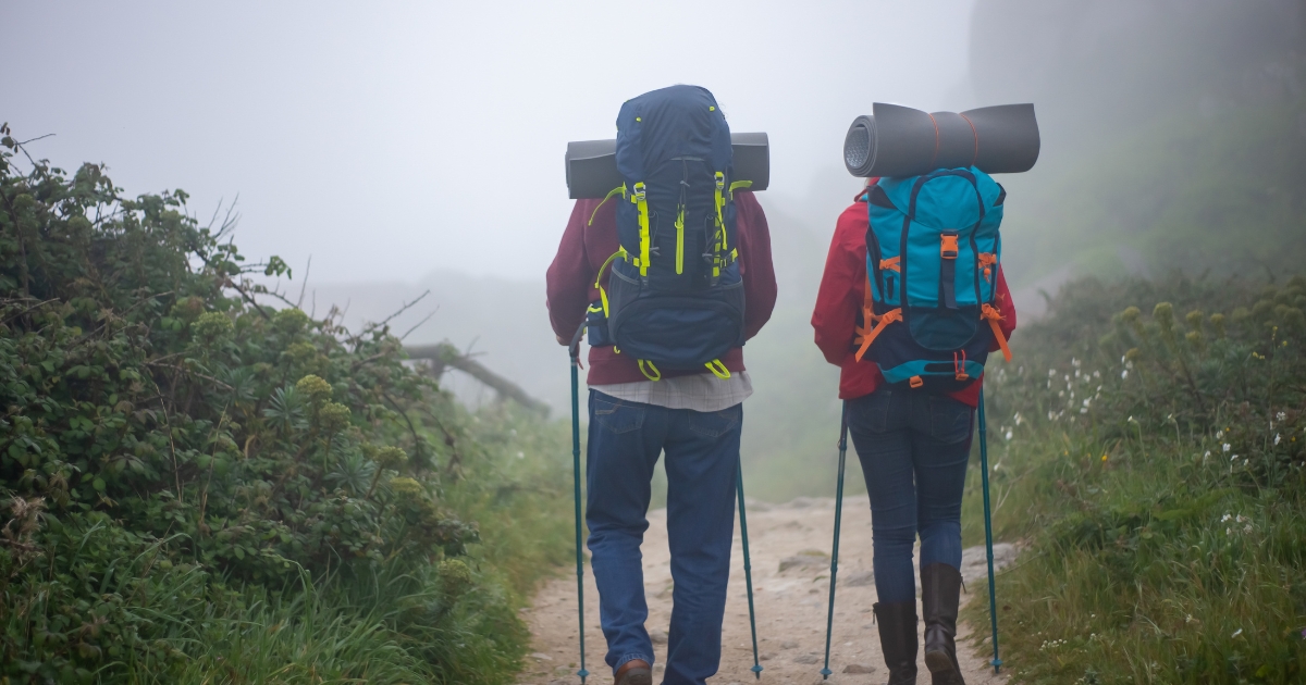Mature couple hiking on a foggy mountain trail with backpacks and trekking poles