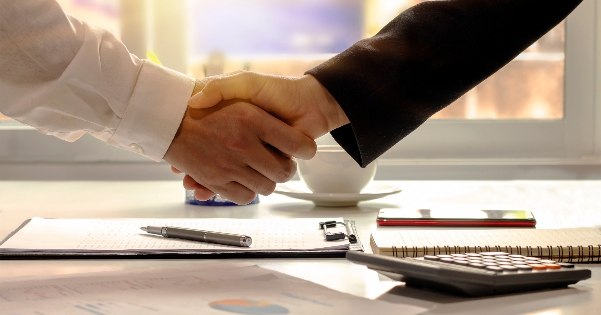Close-up handshake over legal and financial documents, symbolizing prenuptial agreement negotiation.