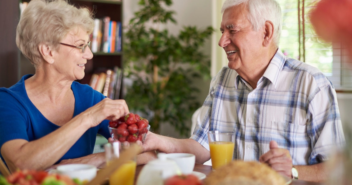 Smiling senior couple enjoying breakfast together at home, sharing strawberries and orange juice in a warm, relaxed setting.