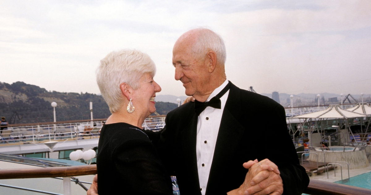 Elegant senior couple dancing and smiling at each other on the deck of a cruise ship, dressed in formal evening attire.