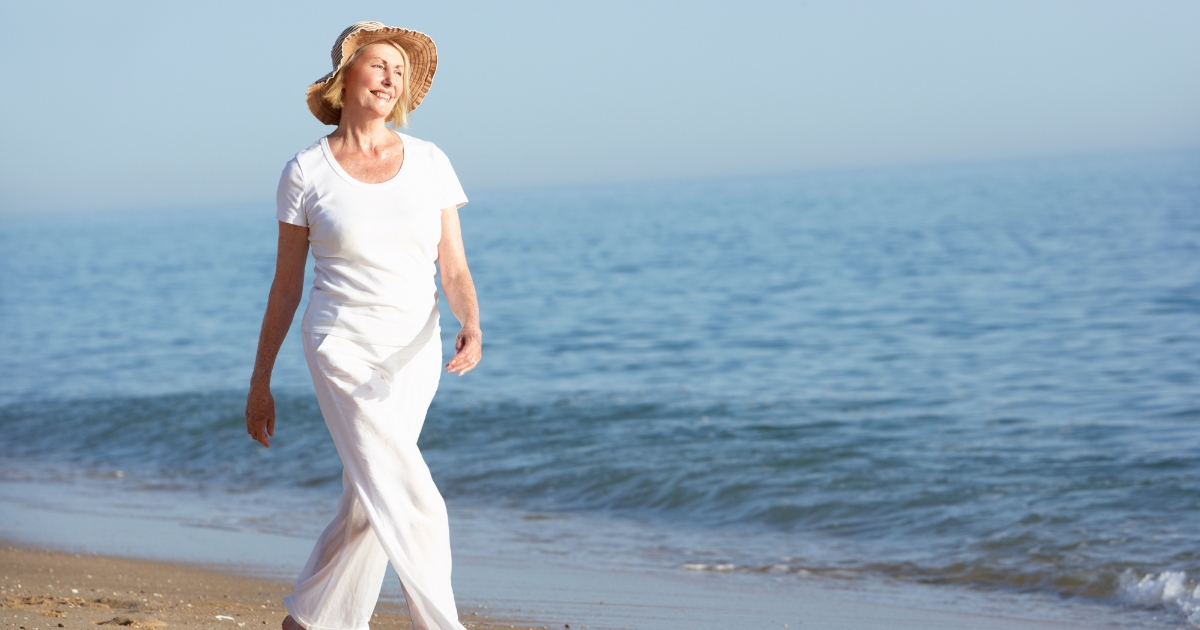 Happy senior woman walking alone on the beach, enjoying independence and freedom in single life after 50.