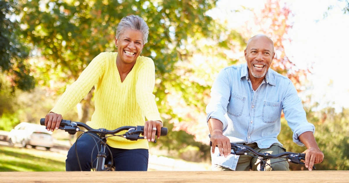Happy senior couple riding bicycles in a sunny park, smiling and enjoying an active lifestyle after 50 – promoting health, confidence, and joyful aging.
