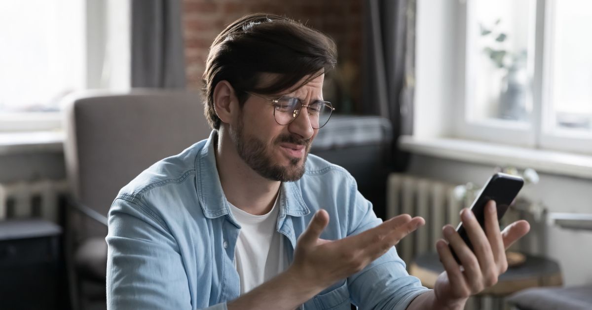 Frustrated man looking at smartphone, confused or disappointed after no response or follow-up after a first date.