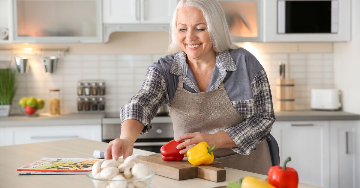 Smiling older woman preparing vegetables in a modern kitchen, enjoying solo living and home cooking.