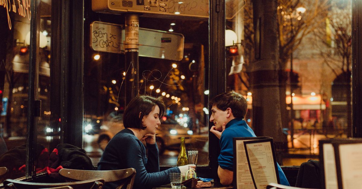 Couple enjoying an intimate dinner date at a cozy restaurant with a city view at night.